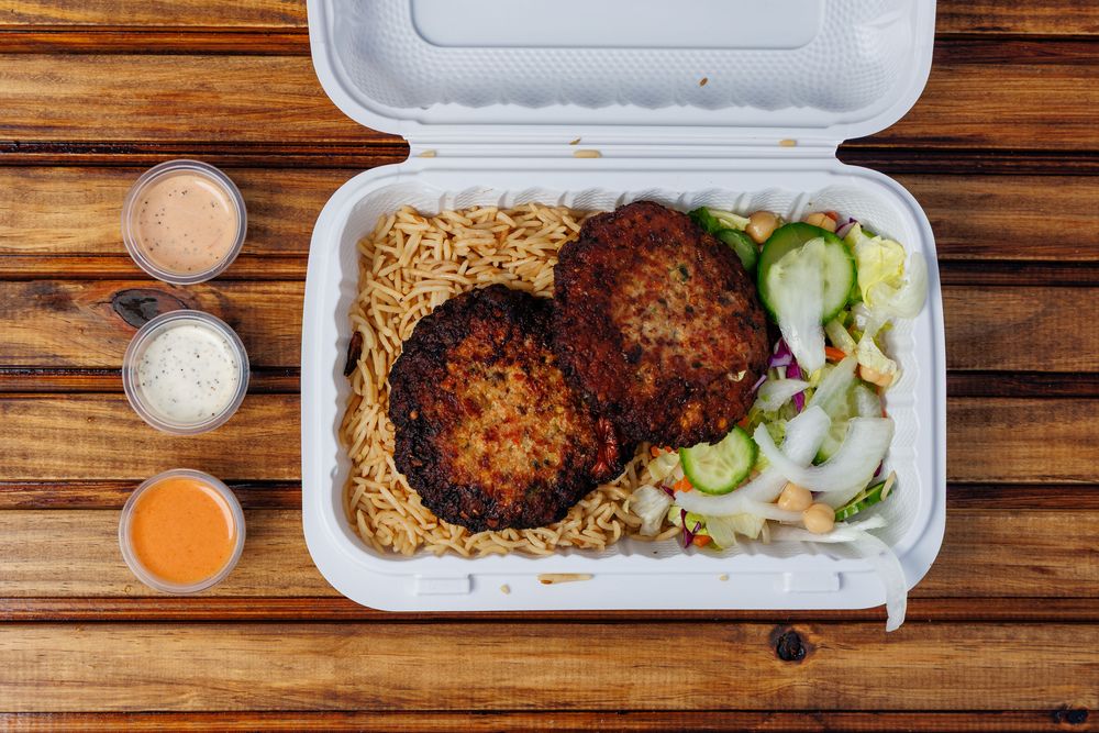 Two chapli kabab patties with dark, crisp edges, served over rice with salad.