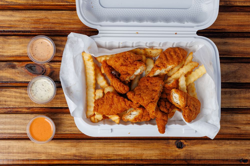 Breaded chicken tenders on crinkle-cut fries in a takeaway box.