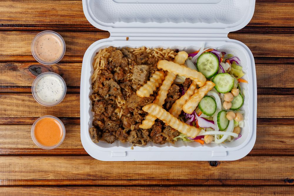 A gyro platter: meat over rice with crinkle-cut fries and salad in a takeaway box.