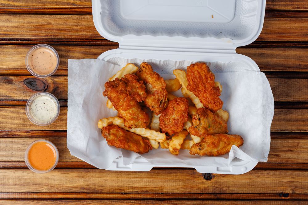 Fried chicken wings piled on crinkle-cut fries in a lined takeaway box.