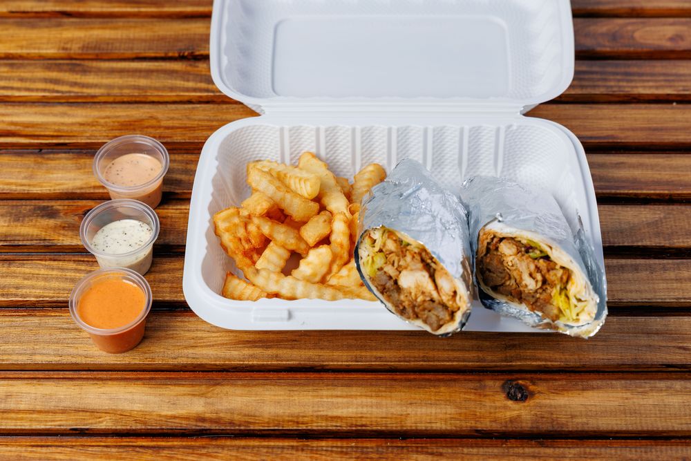 A wrap cut in half in a takeaway box, showing the filling inside flatbread, with crinkle-cut fries alongside.