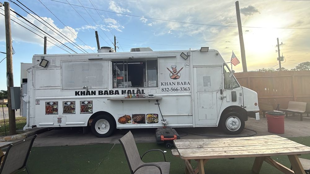 The Khan Baba Halal food truck parked on the lot at sunset, with picnic tables on artificial grass beside it.