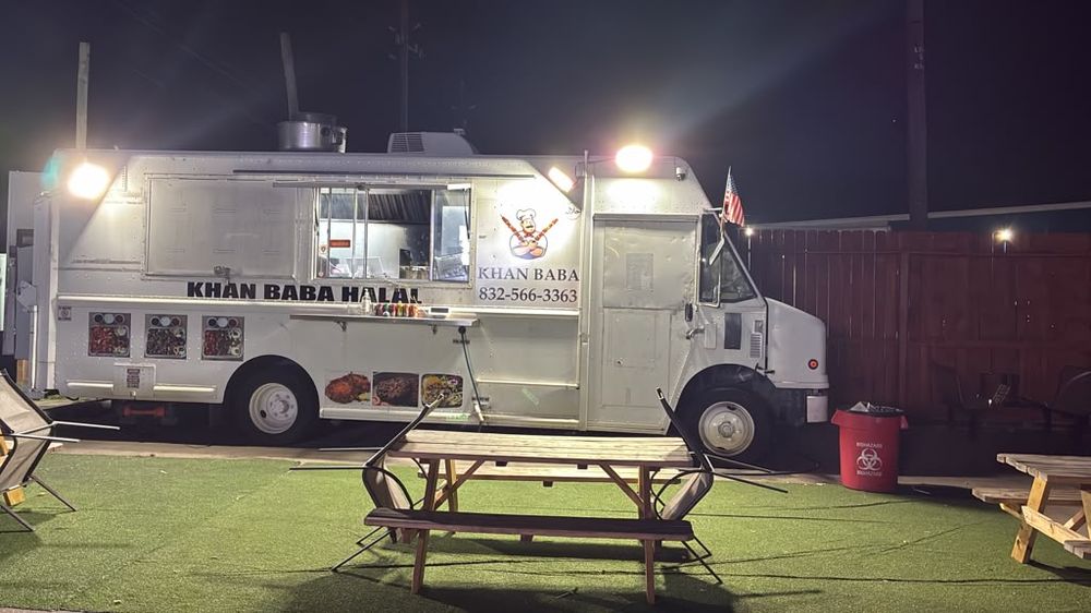 The Khan Baba Halal food truck lit up at night with picnic tables in front.